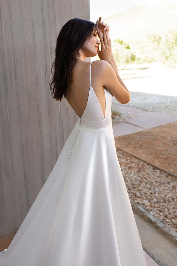 Eine dunkelhaarige Frau im eleganten weißen Rückenfreien Kleid blickt verträumt zurück