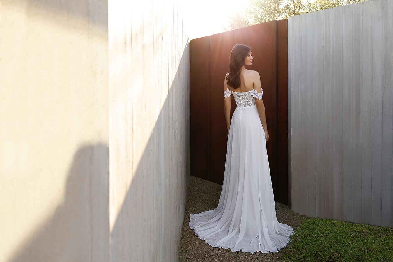Eine Frau im weißen Brautkleid mit offenem Haar steht nachdenklich im Sonnenlicht