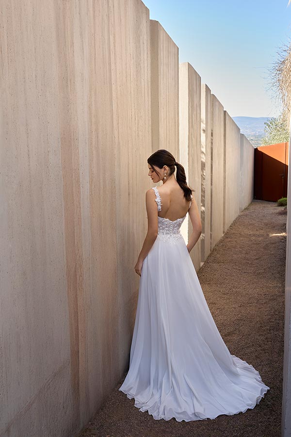 Eine brünette Frau im weißen Spitzenkleid steht mit dem Rücken zur Kamera im Sonnenlicht