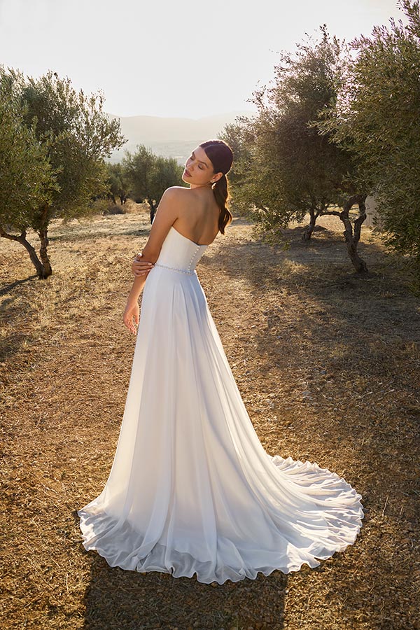 Eine Frau lächelt entspannt in einem weißen Brautkleid auf einem Feld im Sonnenlicht