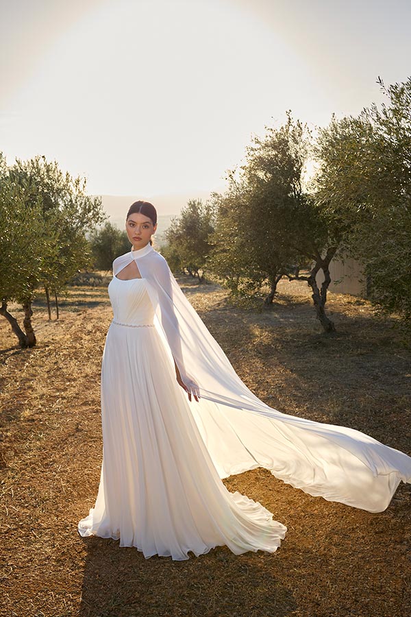 Eine junge Frau mit ernstem Blick trägt ein weißes, fließendes Kleid im Sonnenschein