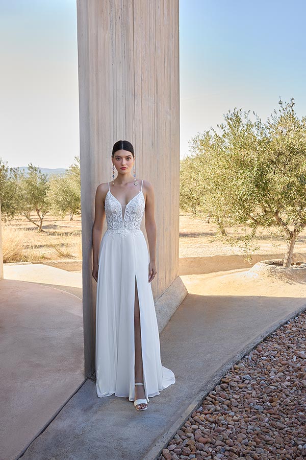 Eine Frau mit ernstem Blick trägt ein weißes Brautkleid mit Schlitz und Spitze