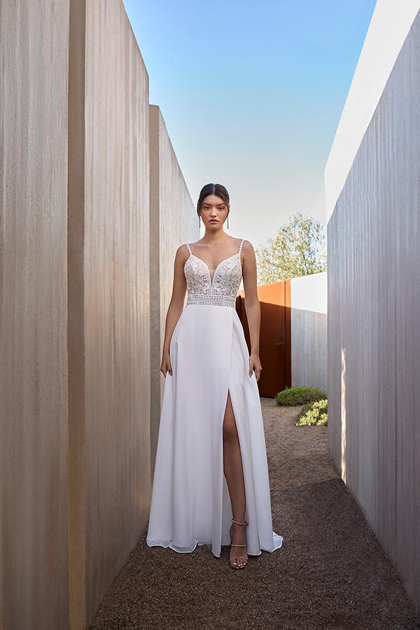 Junge Frau mit ernstem Blick trägt ein elegantes weißes Kleid mit Spitzenoberteil und Beinschlitz
