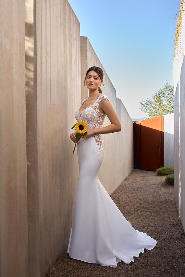Junge Frau im eleganten Brautkleid hält eine Sonnenblume und wirkt nachdenklich