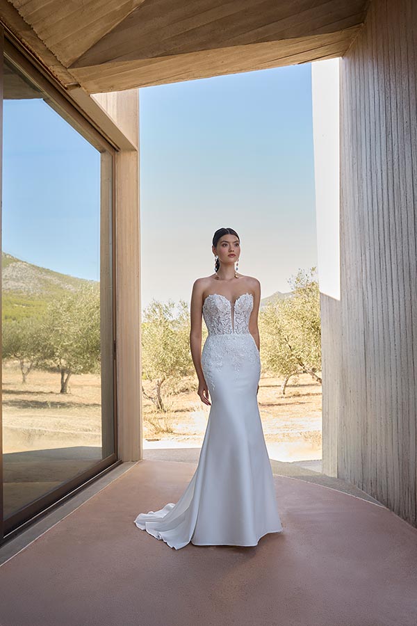 Eine junge Frau in einem weißen Brautkleid mit Spitzenoberteil steht elegant draußen