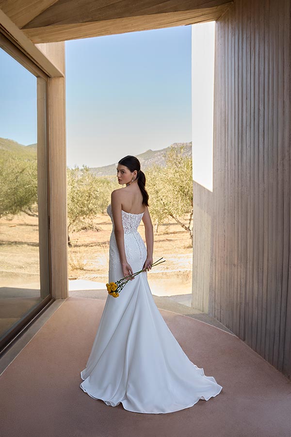 Eine junge Frau im eleganten weißen Brautkleid hält gelbe Blumen und blickt ernst