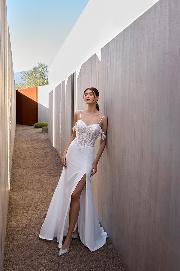 Eine junge Frau mit elegantem weißen Kleid und Spitze steht entspannt an einer Mauer