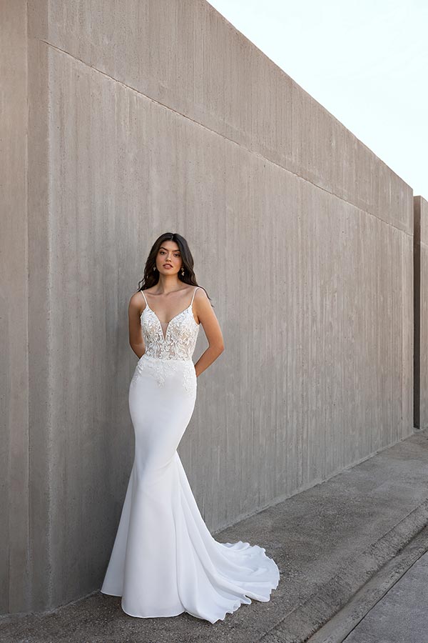 Eine junge Frau mit ernstem Blick trägt ein elegantes weißes Spitzenkleid vor Betonwand