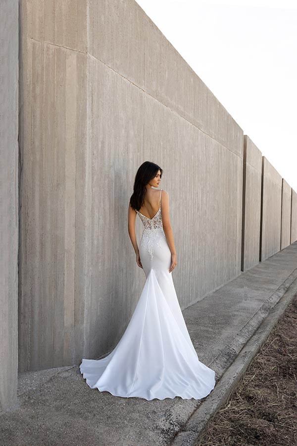 Eine Frau mit dunklem Haar trägt ein elegantes weißes Kleid und blickt zurück