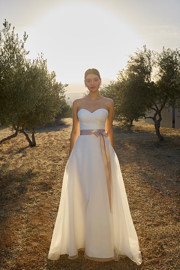 Eine junge Frau mit ernstem Blick trägt ein elegantes weißes Brautkleid im Sonnenschein