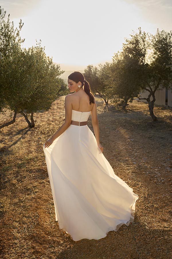 Eine Frau mit eleganter Pose im weißen Kleid steht auf einem sonnigen Feldweg