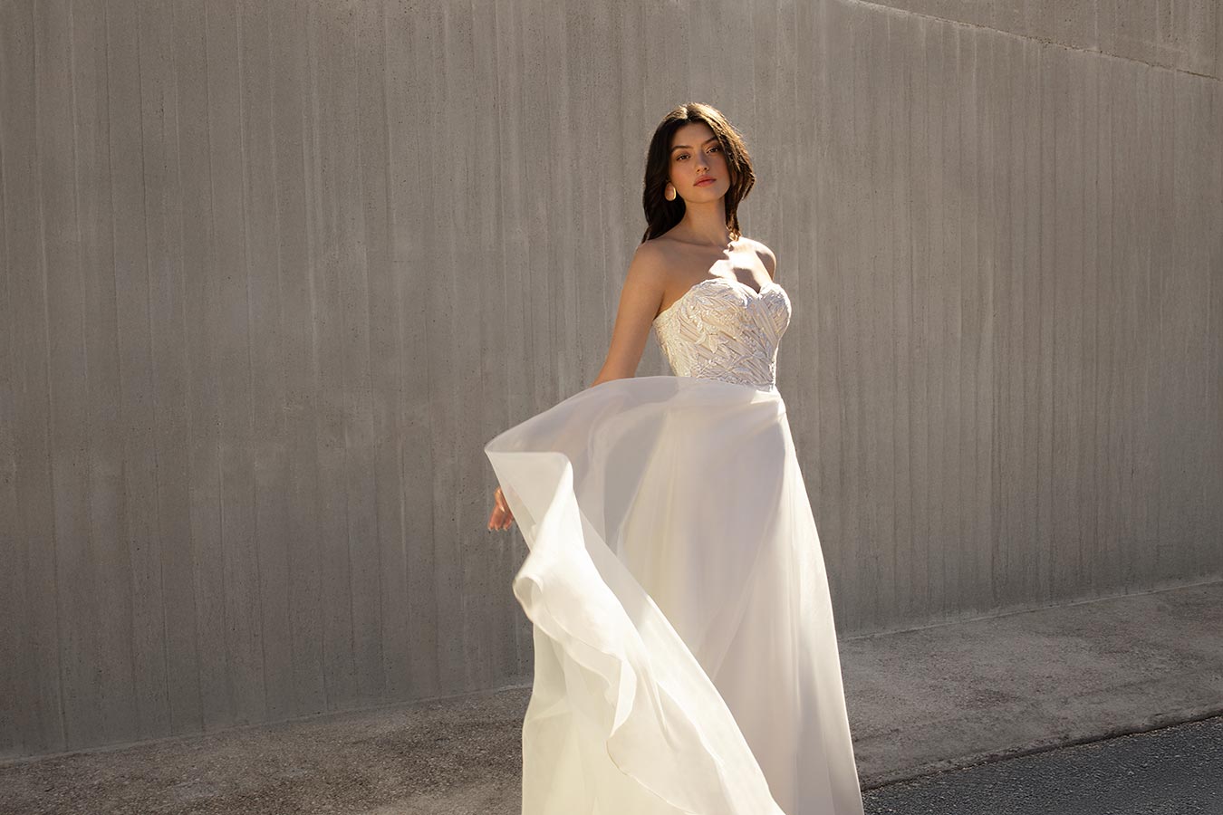 Eine Frau mit ernster Miene trägt ein weißes Brautkleid und hält den Rock hoch