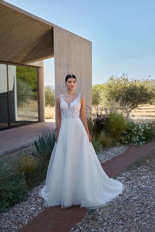Junge Frau mit ernstem Blick trägt ein weißes, elegantes Brautkleid mit Spitze draußen