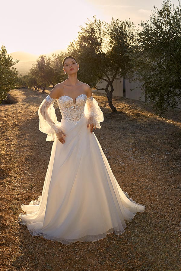 Eine Frau mit ernstem Blick trägt ein elegantes weißes Brautkleid mit Spitzenärmeln