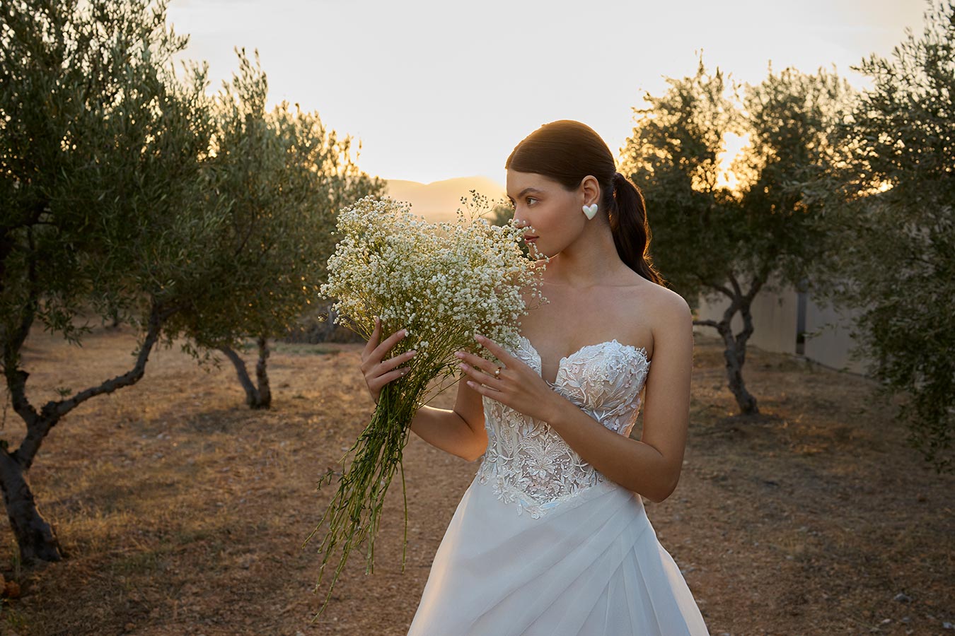 Eine braunhaarige Frau im weißen Brautkleid hält lächelnd einen Schleierkrautstrauß
