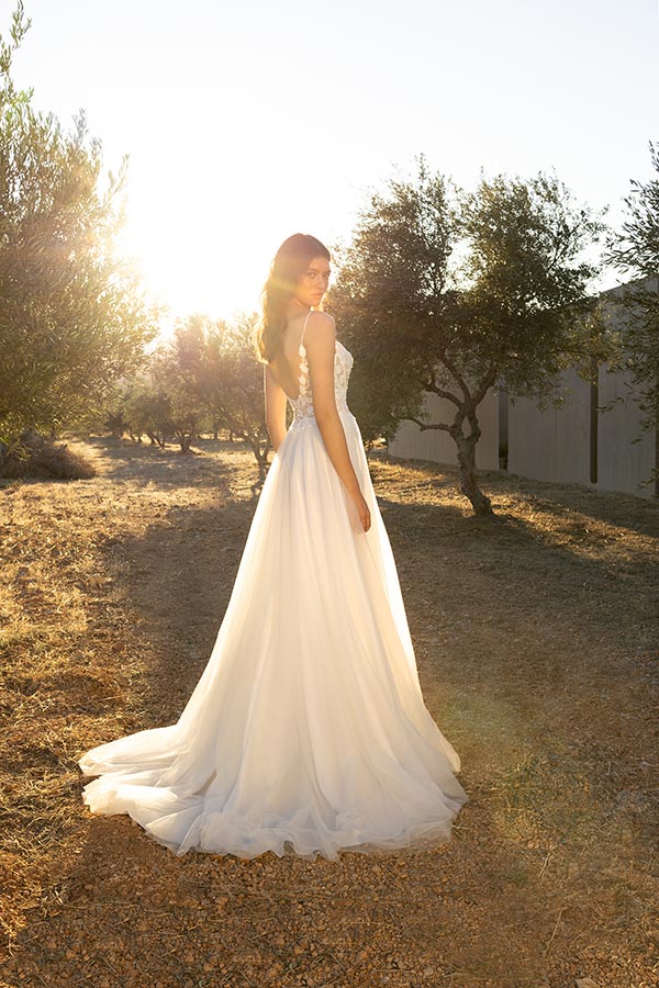 Eine lächelnde Frau im weißen Brautkleid steht in der Sonne auf einem Feldweg