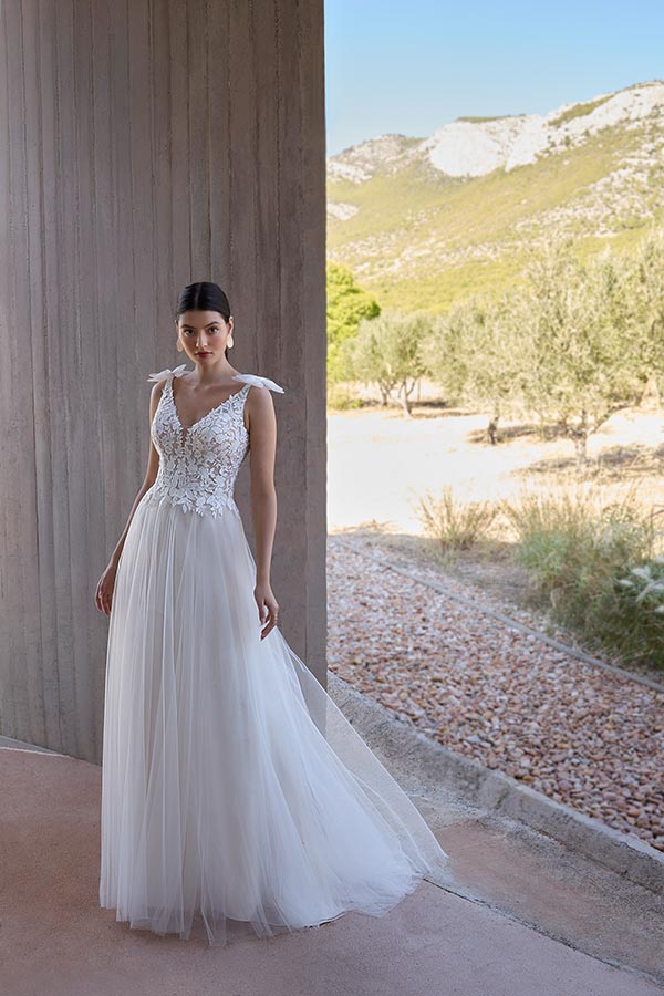 Eine junge Frau mit ernstem Blick trägt ein weißes Brautkleid mit Spitzenmuster