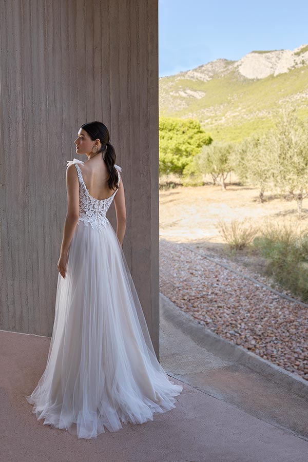 Eine Frau mit dunklen Haaren trägt ein weißes, elegantes Brautkleid und blickt ruhig