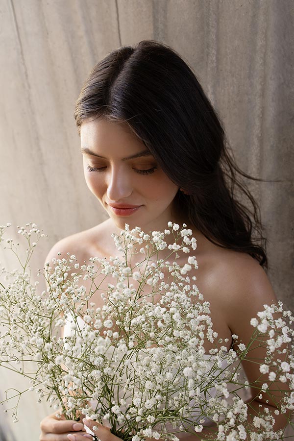 Eine junge Frau mit langen dunklen Haaren lächelt sanft und hält zarte Blumen in Weiß