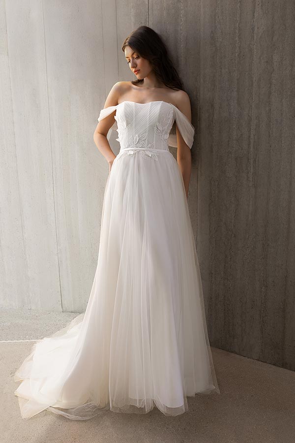 Eine junge Frau im cremefarbenen Brautkleid steht lächelnd an einer Betonwand