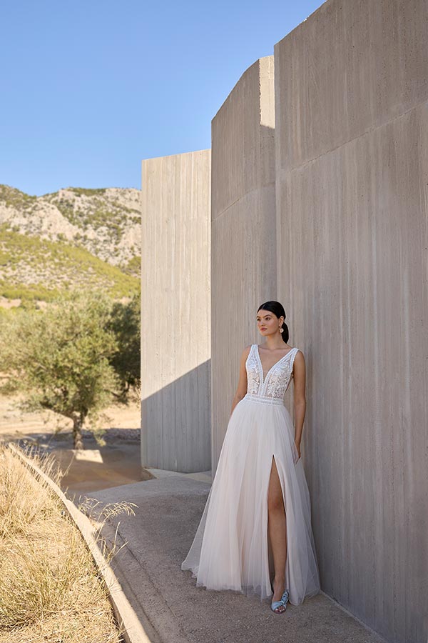 Eine Frau im eleganten weißen Kleid lehnt entspannt an einer Betonwand im Sonnenschein