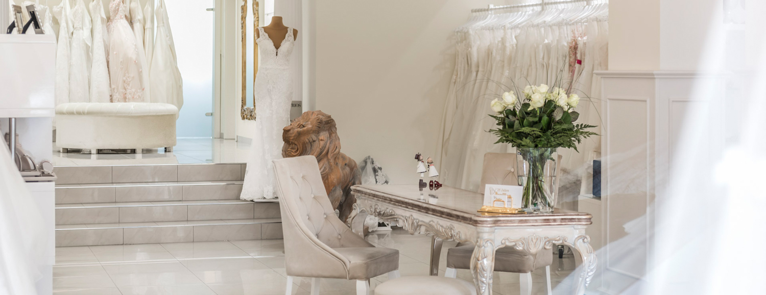 Ein eleganter, heller Brautmodenladen mit cremefarbenen Kleidern und Blumen auf dem Tisch