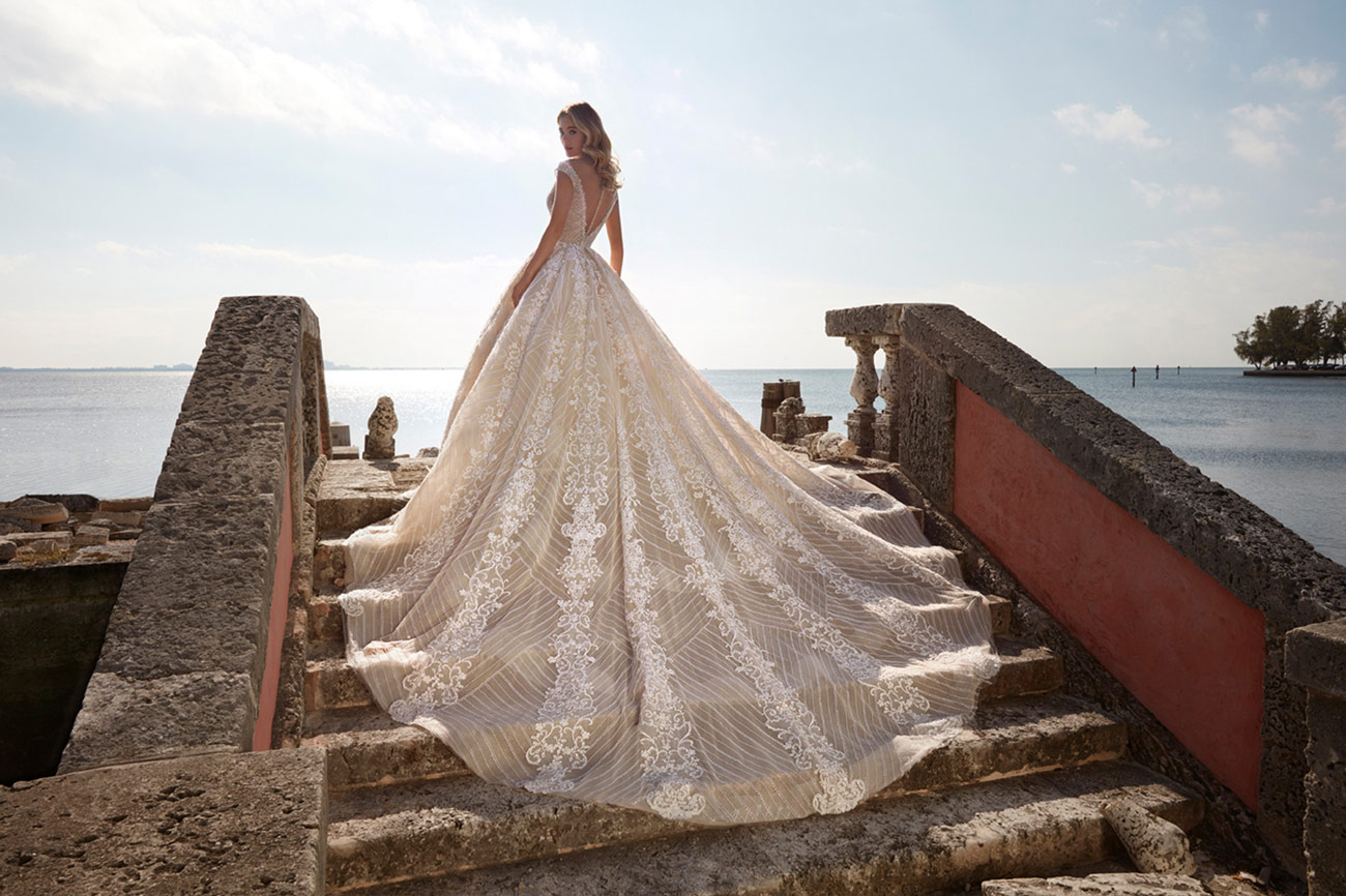 Eine Frau im eleganten cremefarbenen Brautkleid steht auf Steinstufen am Wasser