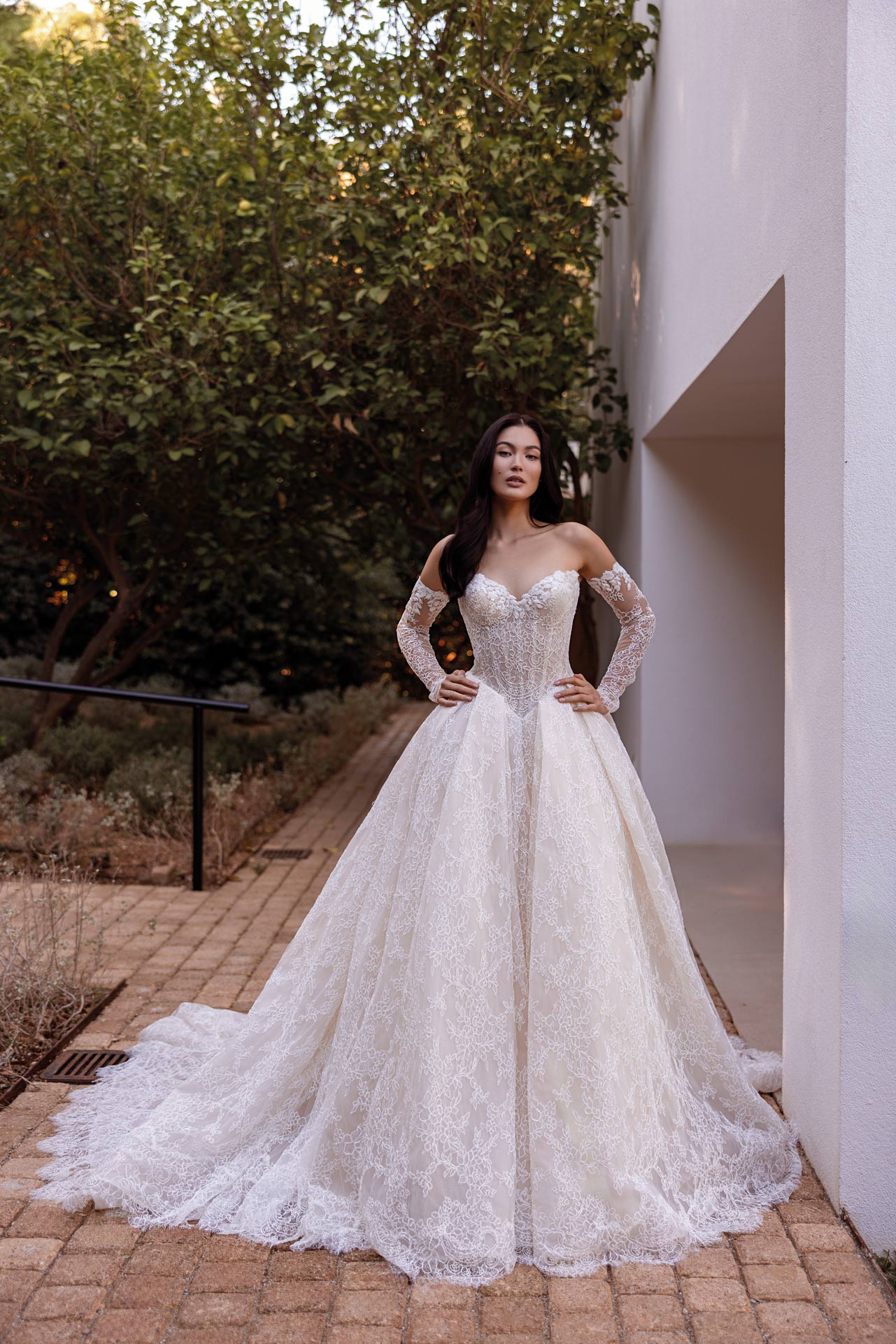 Selbstbewusste Braut in einem eleganten weissen Spitzenkleid vor einer Wand