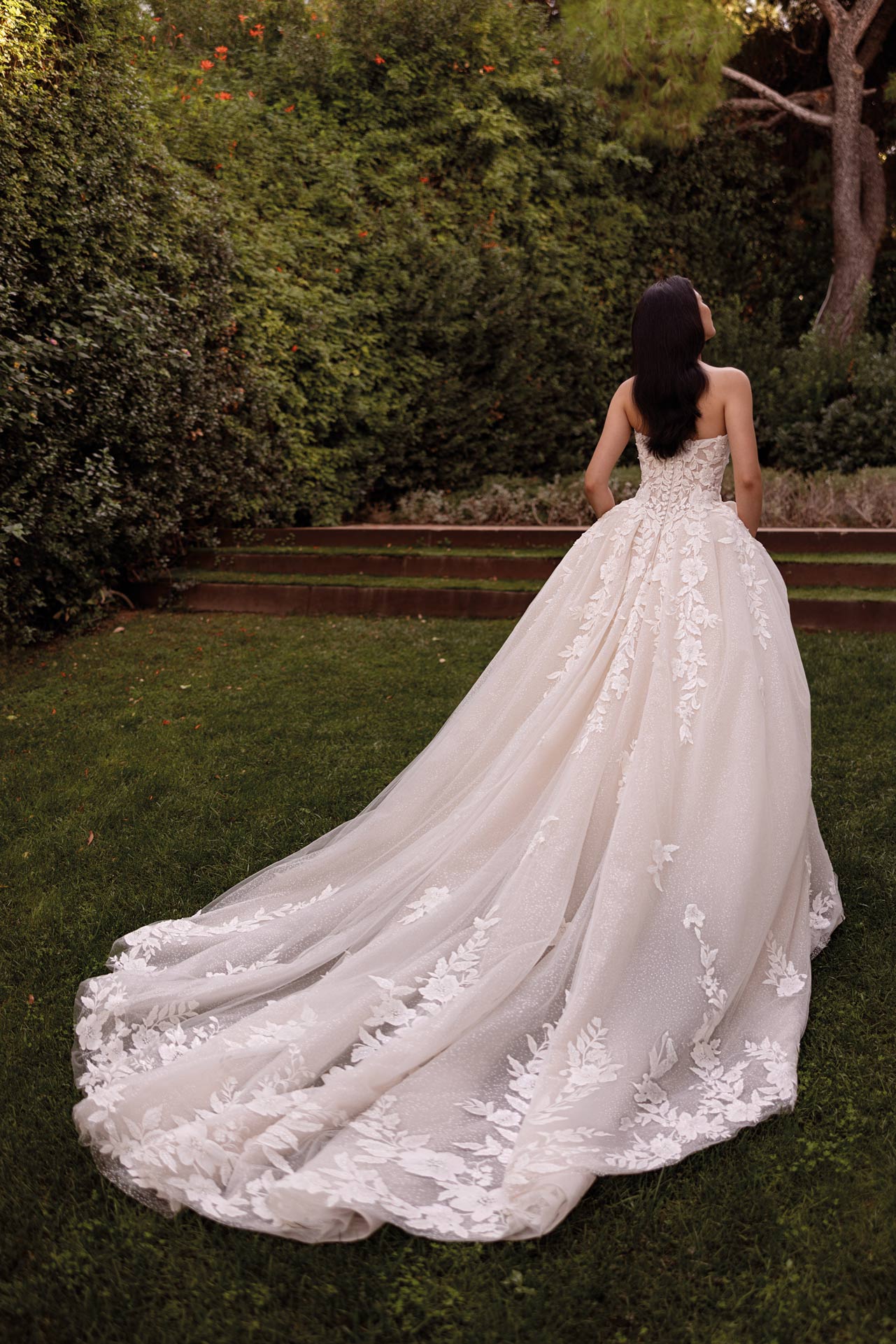 Braut mit dunklem Haar im weissen Spitzenkleid mit langer Schleppe im Garten