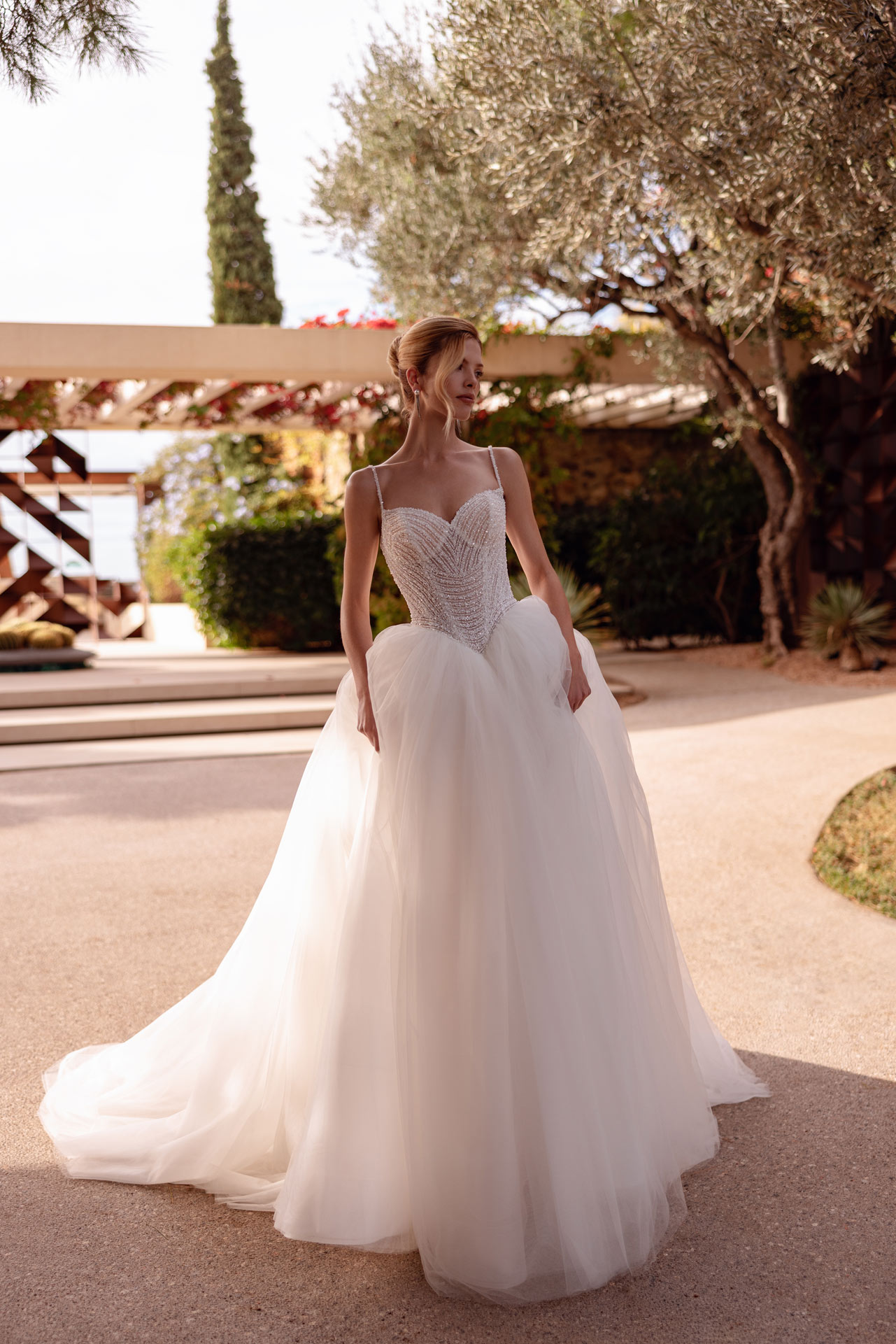Blonde Frau im weissen Brautkleid mit Perlenkorsage und Tuellrock im Garten