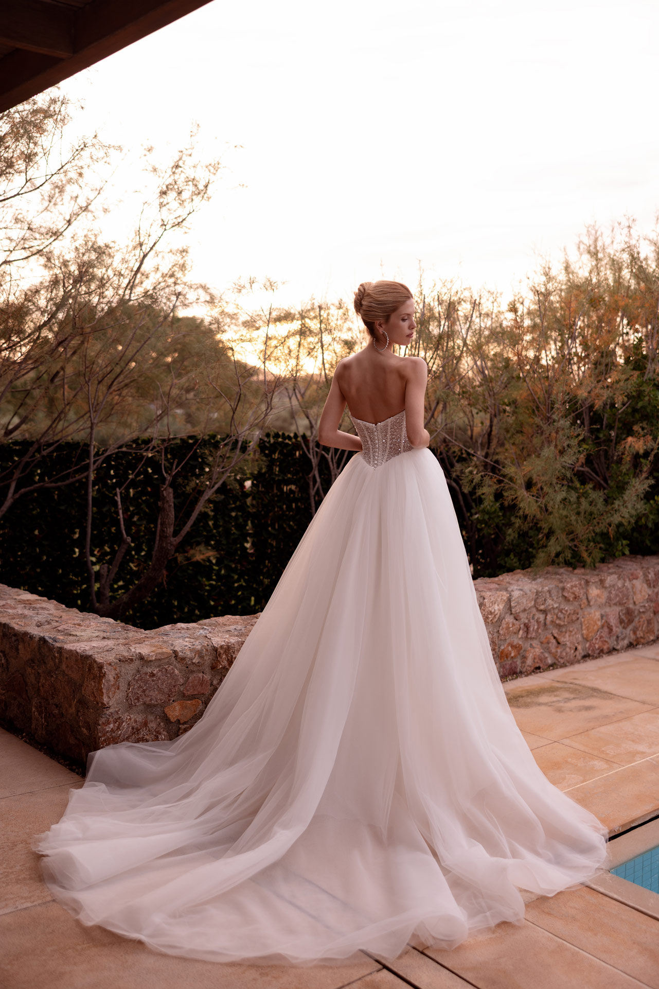 Braut mit hochgestecktem Haar traegt ein weisses Tuellkleid mit Schleppe