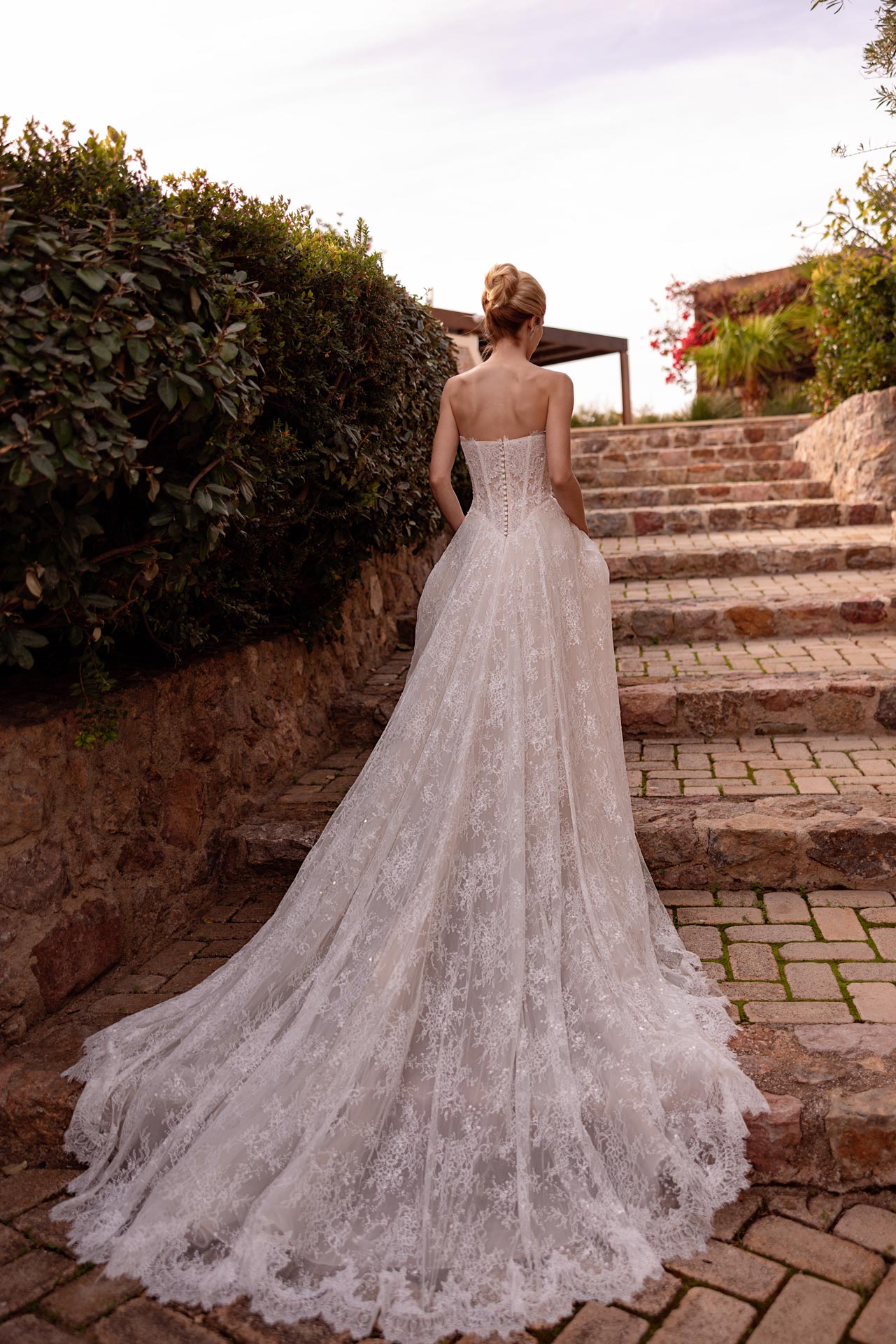 Blonde Braut im weissen Spitzenkleid mit langer Schleppe auf Steintreppe