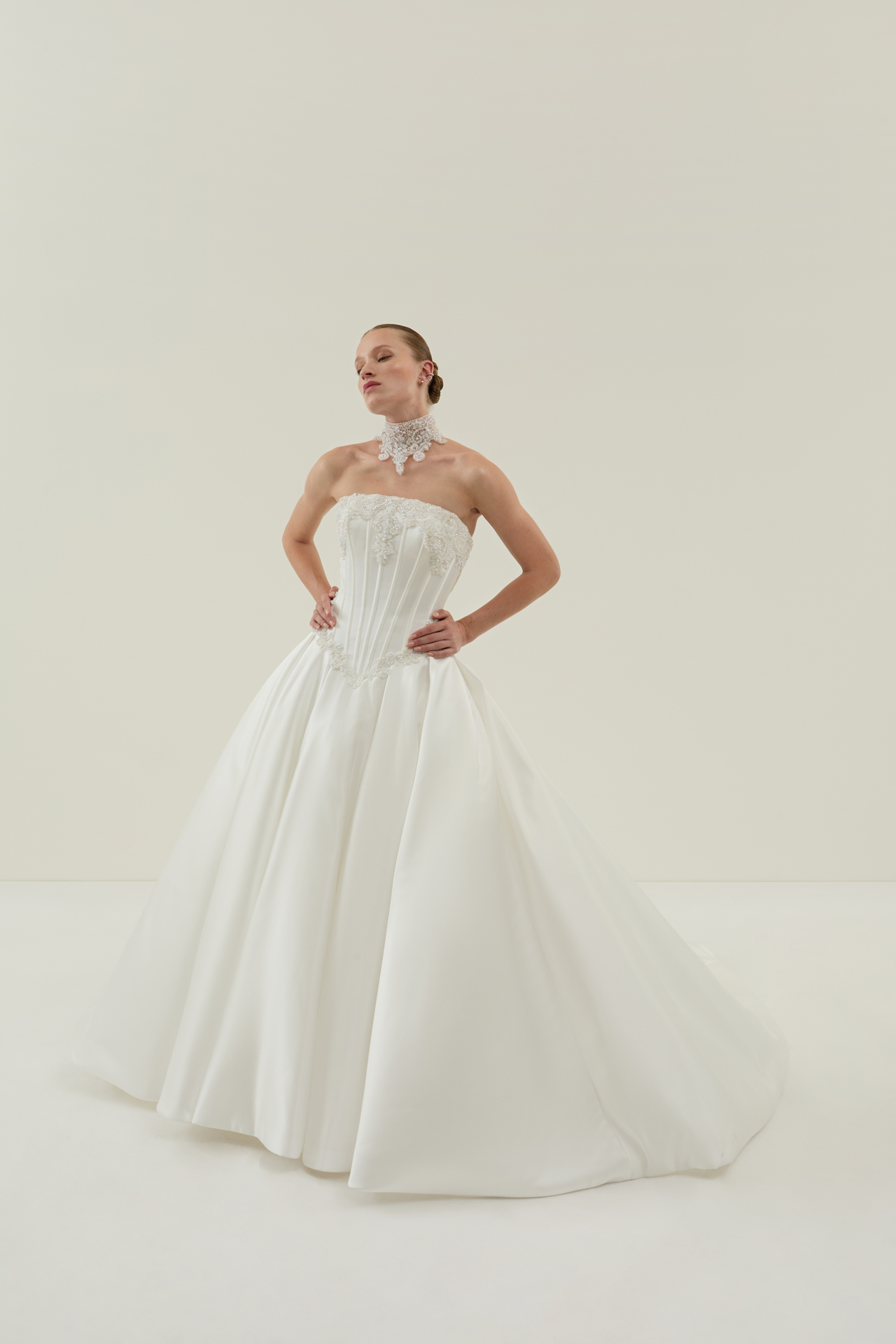 Elegante Frau in weissem Brautkleid mit Perlenhalsband posiert selbstbewusst