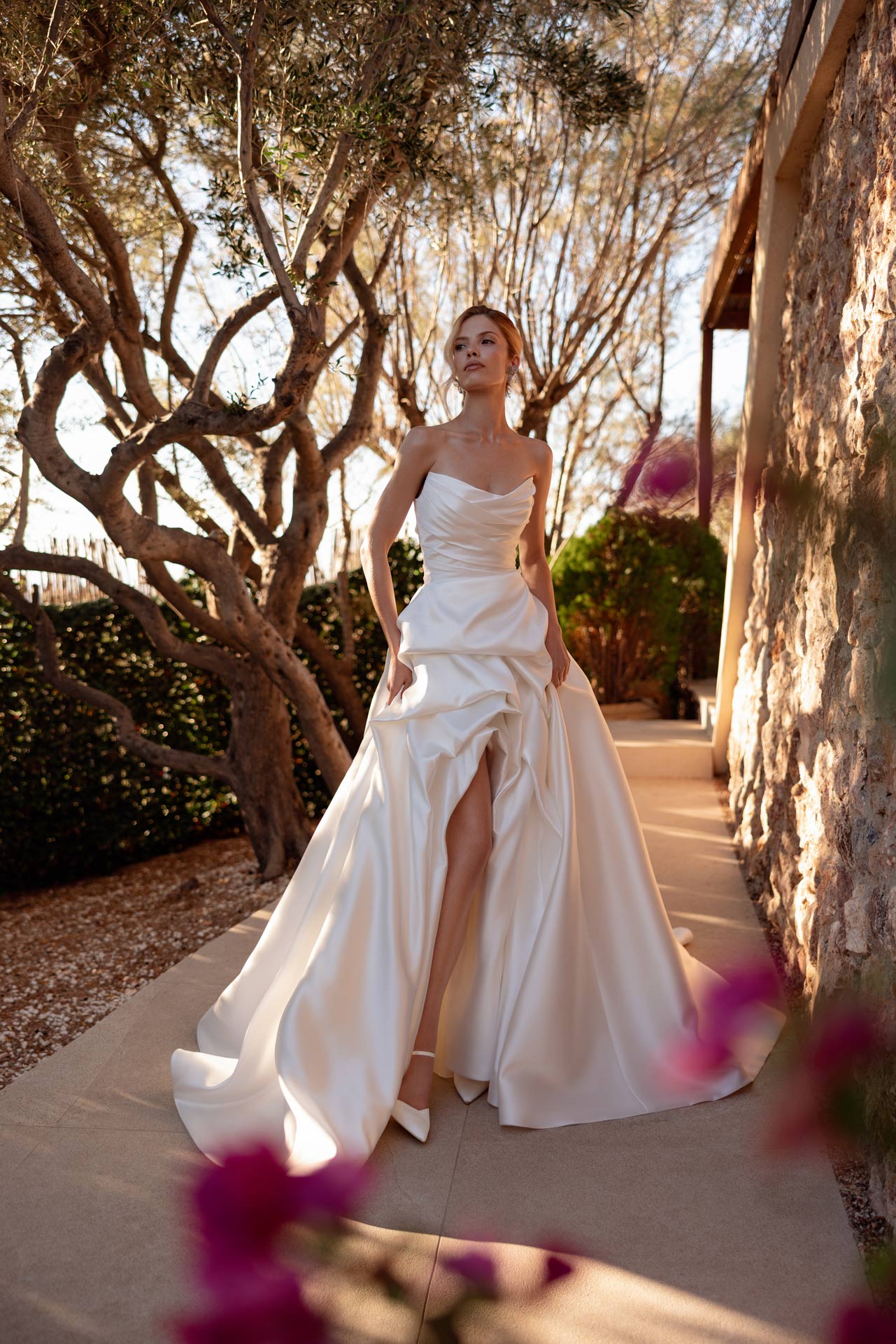 Junge blonde Frau im eleganten cremefarbenen Brautkleid im sonnigen Garten
