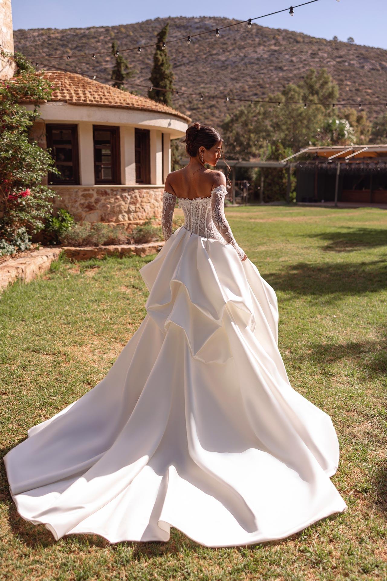 Braut im weissen Spitzenkleid mit langer Schleppe im sonnigen Garten