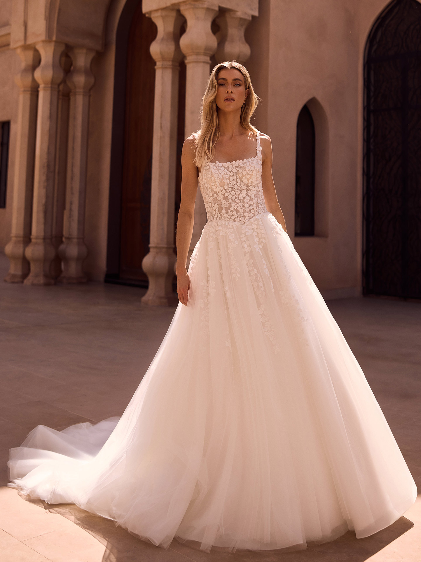 Blonde Frau im weissen Brautkleid mit Spitze und Tuellrock schaut ernst